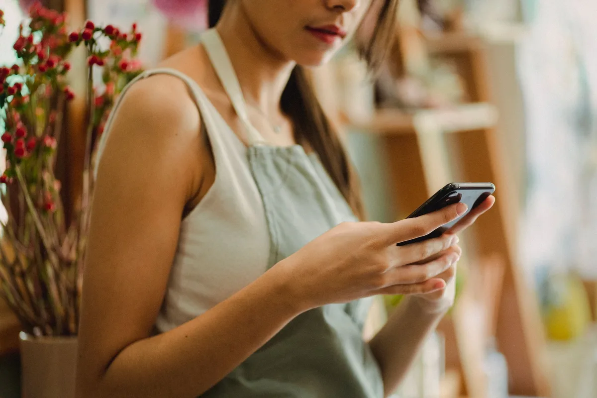 Winkelier met een schort voor leest berichten op haar telefoon
