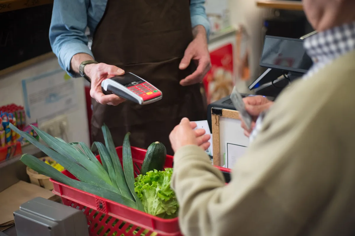 Klant houdt zijn pas bij de betaalautomaat aan een kraam met groentekratten